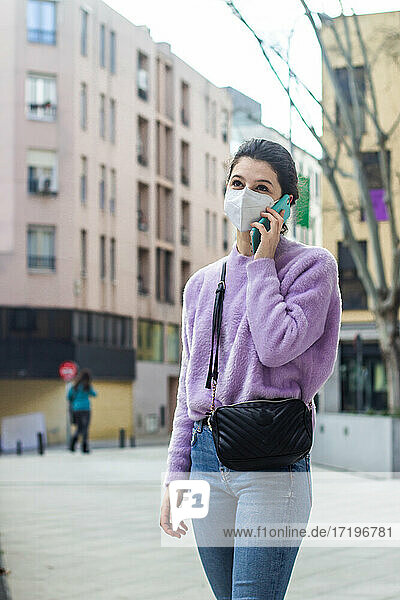 junge Frau mit KN95-Schutzmaske auf der Straße  die mit dem Handy spricht