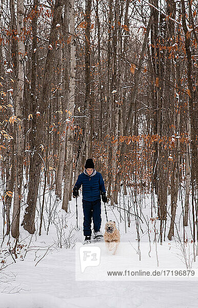 Teen boy snowshoeing with dog in the woods on a snowy winter day.