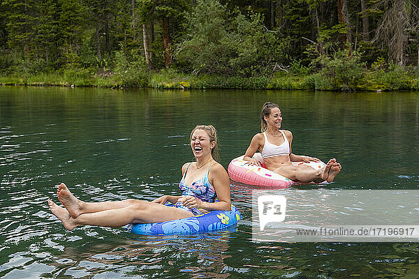 Fröhliche Freundinnen sitzen auf aufblasbaren Ringen im See