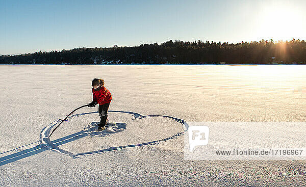 Ein Kind zeichnet ein Herz auf einem verschneiten Feld in der Morgensonne.