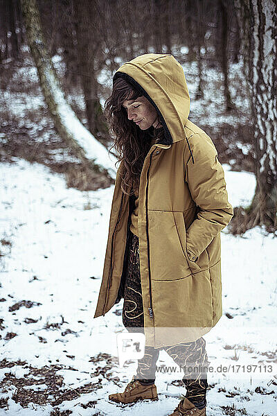 young woman with freckles & long curly hair smiles under hood in snow