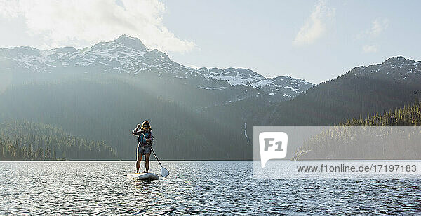 Abenteurerin paddelt auf einem See vor einem verschneiten Bergkamm