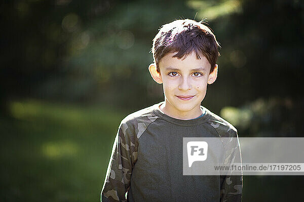 Cute little boy in camo shirt with big brown eyes outdoors.