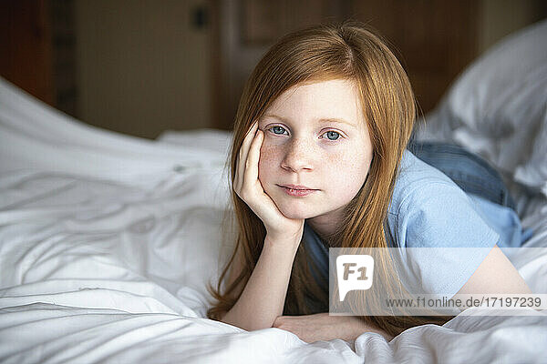 Junges  glückliches  rothaariges  blauäugiges Mädchen liegt auf einem weißen Bett.