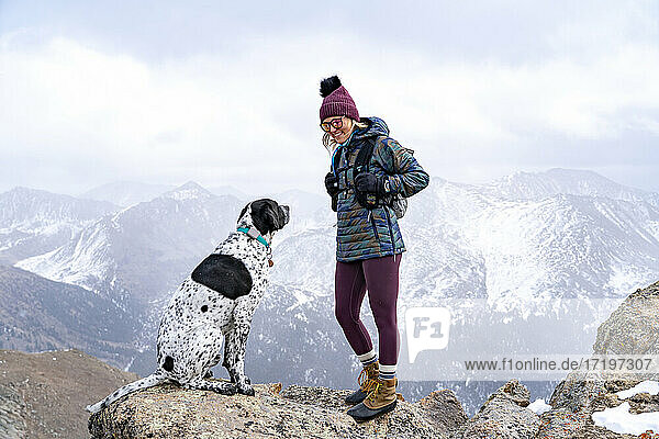 Smiling young woman with Pointer dog on mountain peak while hiking during vacation