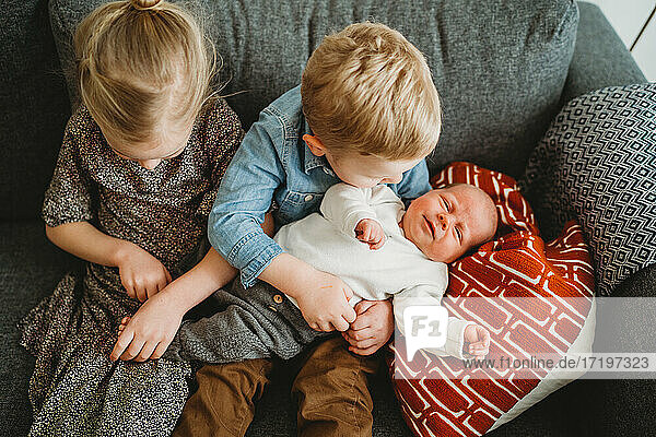 Baby auf der Couch zu Hause mit Bruder und Schwester halten ihn