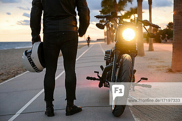 Junger Mann steht in der Nähe von Motorrad und genießt den Sonnenuntergang Blick