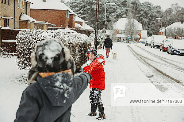 Brüder  die in einer verschneiten Wohnstraße Schneebälle werfen