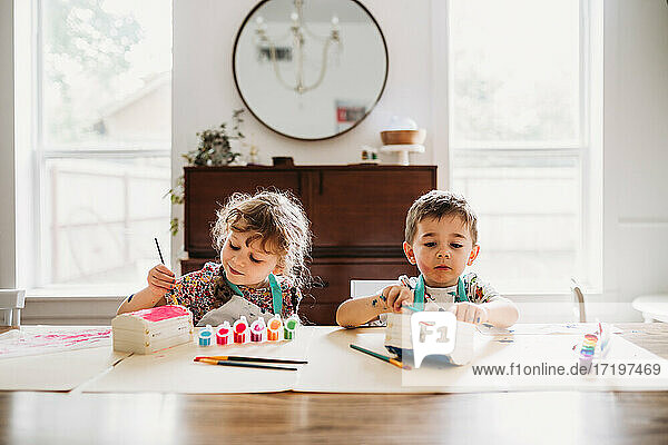Junge Geschwister sitzen und malen bunte Schachteln im modernen Esszimmer