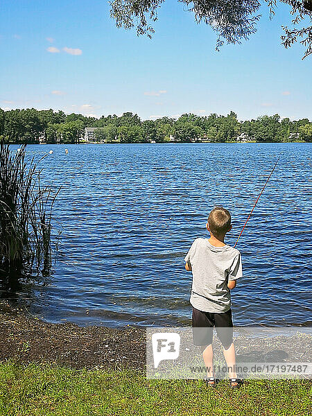 Junge mit Angelrute an einem Teich im Sommer  der seinen Fisch einholt