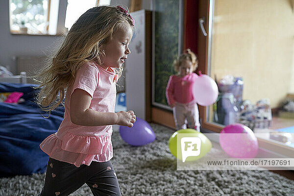 Fröhliches kleines Mädchen  das zu Hause herumläuft und mit seiner Schwester und den Ballons spielt.