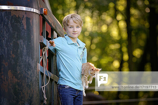 Hübscher blonder Junge hält ein Kätzchen im Freien in ländlicher Umgebung.