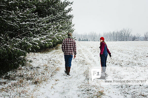 Two Teens Walking Through a Snowy Field with Pines in Michigan