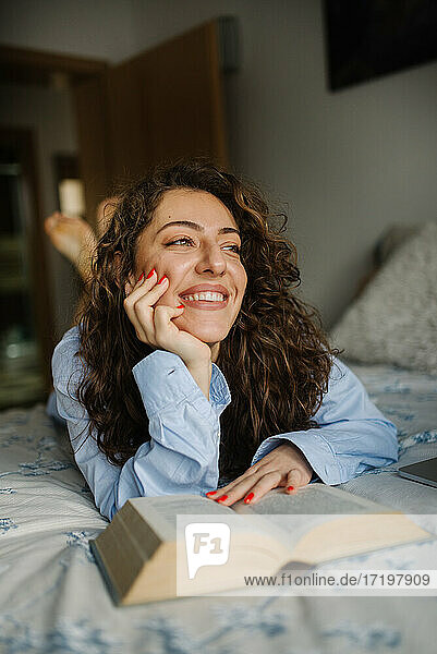 Glückliche junge Frau  die im Bett liegend ein Buch liest.