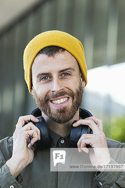 Lächelnder Mann mit Kopfhörern um den Hals vor einem Gebäude
