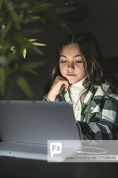 Mädchen mit braunem Haar studiert durch digitale Tablette am Tisch in der Wohnung