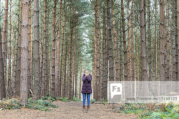 Frau in warmer Kleidung inmitten von Bäumen im Wald stehend