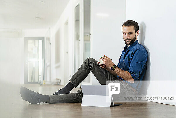 Junger Geschäftsmann schaut auf ein digitales Tablet  während er im Büro etwas isst