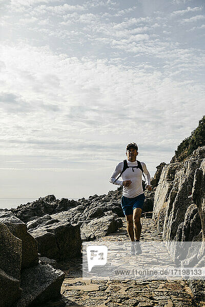 Mature man running on footpath between rock formations against cloudy sky