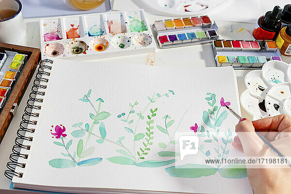 Frau malt botanische Pflanzen und Blumen auf Papier am Tisch