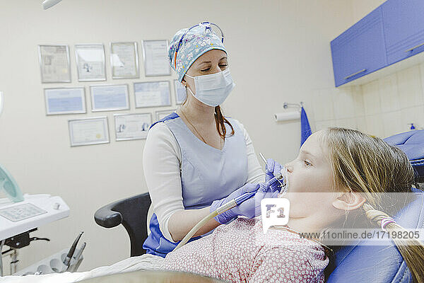 Zahnärztin mit Gesichtsschutzmaske bei der Untersuchung eines kleinen Mädchens im Büro