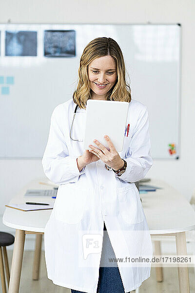 Smiling medical worker using digital tablet while standing against desk