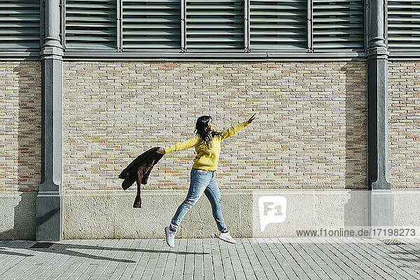 Frau mit Jacke springt auf dem Gehweg an der Mauer