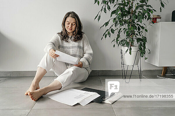 Unternehmerin liest Dokumente  während sie zu Hause an der Wand sitzt