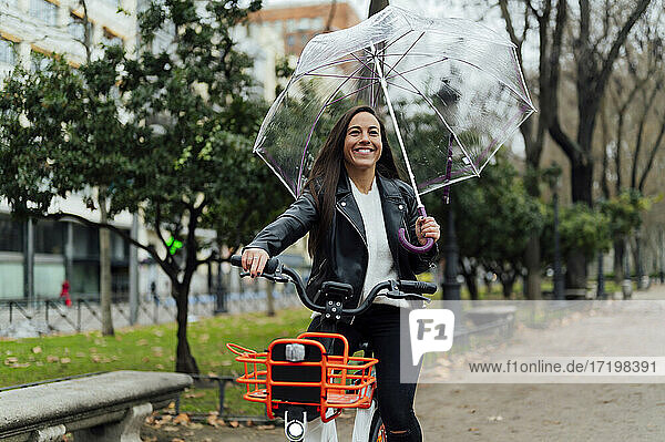 Schöne Frau fährt Elektrofahrrad und hält Regenschirm auf der Straße in der Stadt