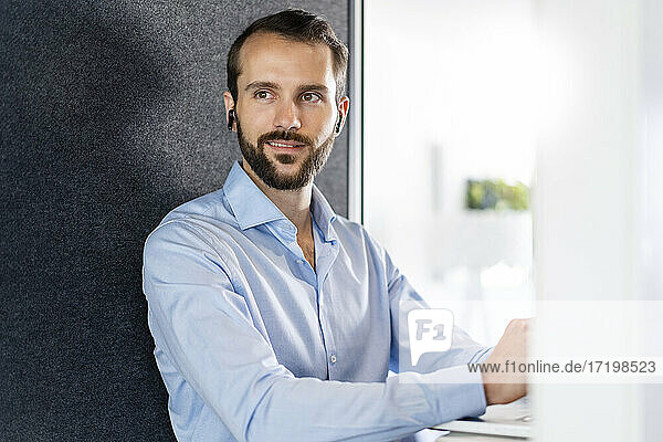 Smiling businessman with in-ear headphones sitting at office