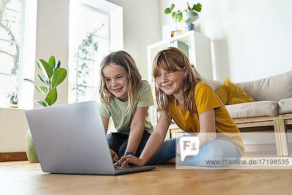Smiling girls using laptop while sitting on floor at home