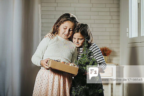 Mädchen mit Kiefer Weihnachten umarmt Schwester hält Weihnachtsschmuck Box zu Hause