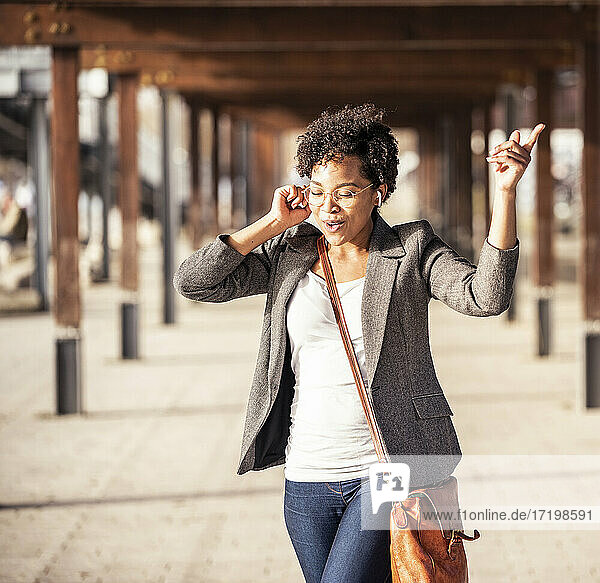 Junge Frau tanzt beim Hören von Musik auf dem Fußweg