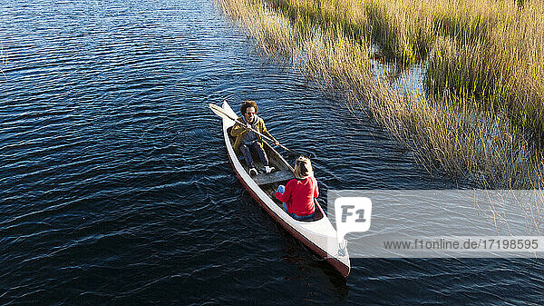 Man with oar paddling while sitting with woman in canoe on river