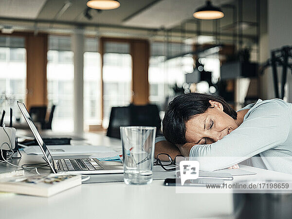 Geschäftsfrau mit gesenktem Kopf  die sich auf dem Schreibtisch im Büro entspannt