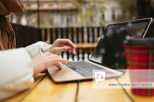 Woman using laptop while sitting at sidewalk cafe