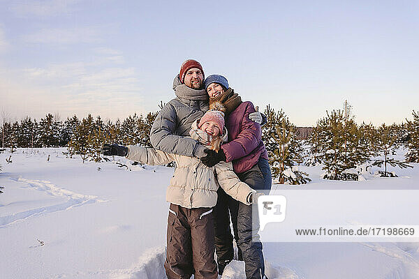 Happy family in warm clothing standing on snow against sky during winter