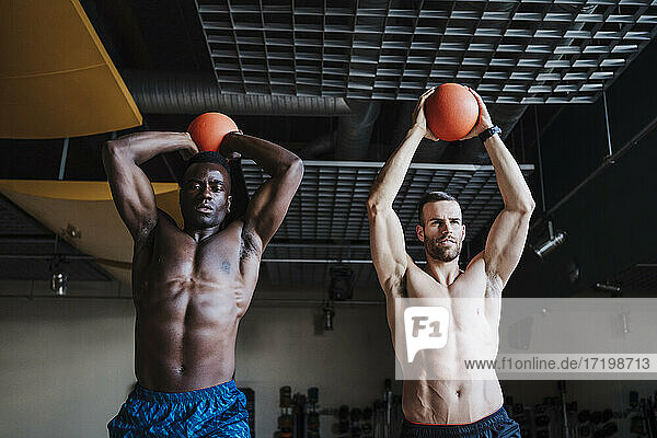 Muscular male athletes holding sports ball while exercising in health club