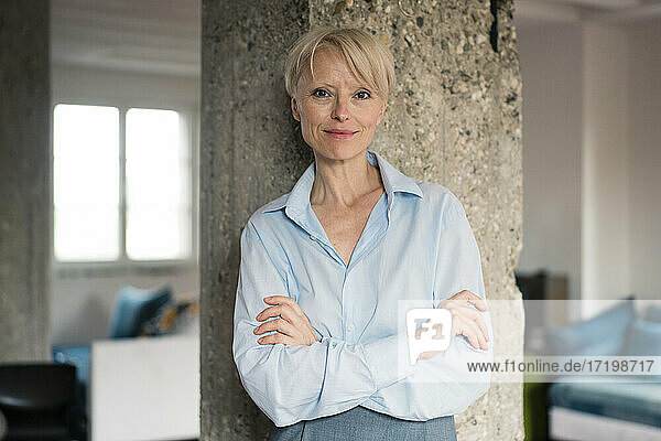 Smiling businesswoman with arms crossed leaning on column at home