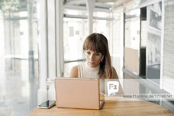 Frau mit Pony arbeitet am Laptop in einem Café