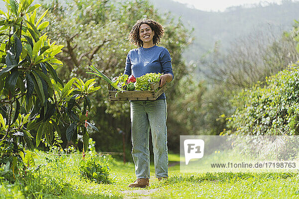 Lächelnde Frau mit Gemüsekiste im Garten stehend