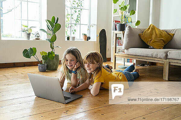 Smiling female friends looking at laptop while lying on front in living room
