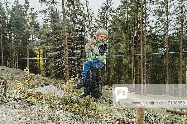 Junge sitzt auf einer Reifenschaukel im Wald während der Ferien im Salzburger Land  Österreich