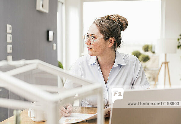 Geschäftsfrau mit Brille sitzt am Schreibtisch und schaut weg