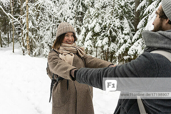 Young woman smiling while holding hands of man standing in forest
