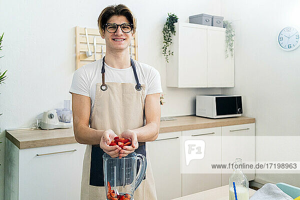 Lächelnder junger Mann gibt gehackte Erdbeeren in den Mixer