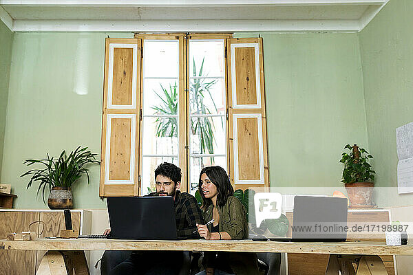 Male and female design professionals working on laptop at desk in industry