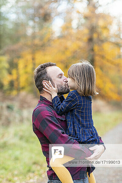 Vater küsst Tochter im Wald stehend