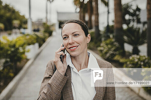 Smiling female entrepreneur talking on phone looking away