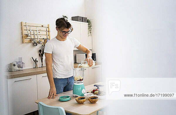 Mann mit Brille gießt Milch in den Mixer  während er in der Küche einen Smoothie zubereitet